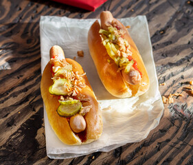 two hot dog buns with sausages pickles fried onions ketchup and mustard bottle on the table