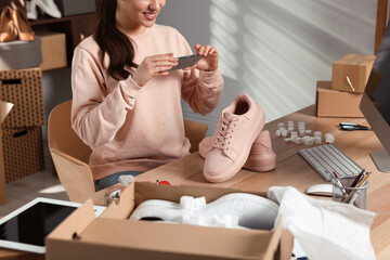 Shoes seller taking picture of pink sneakers at table in office, closeup. Online store