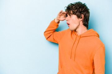 Young caucasian man isolated on blue background looking far away keeping hand on forehead.