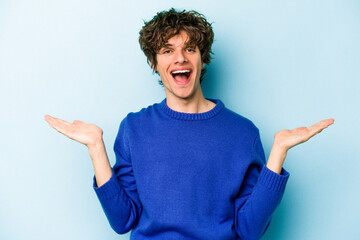 Young caucasian man isolated on blue background makes scale with arms, feels happy and confident.