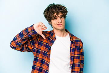 Young caucasian man isolated on blue background showing a dislike gesture, thumbs down....
