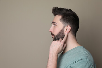 Man pointing at his ear on grey background. Space for text