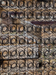 close up abstract of mattress bed springs used as outdoor outside fence see through spirals and different sized circular springs in rows and columns pattern colored vertical backdrop or background