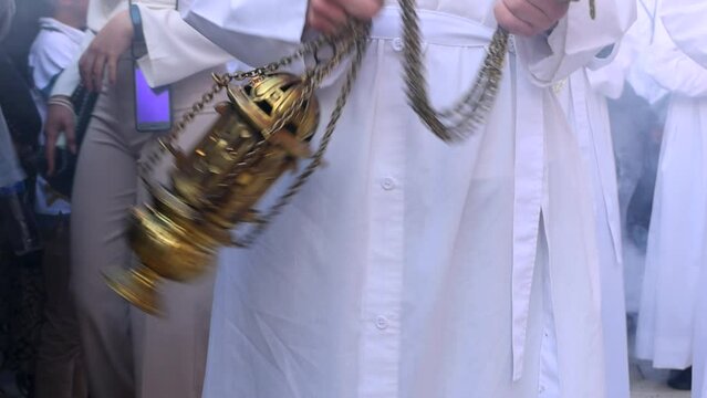 Altar boy or acolyte in the holy week procession shaking a censer to produce smoke and fragrance of incense