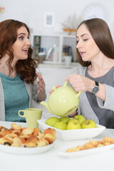 Portrait of two smiling female friends sitting at table and drinking tea