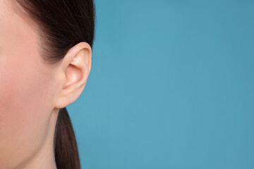 Woman on light blue background, closeup of ear. Space for text - obrazy, fototapety, plakaty