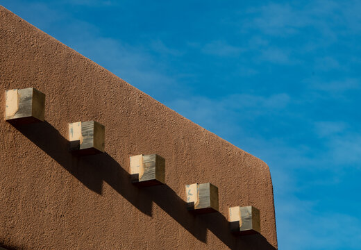 shadows of beams of adobe house cast onto rust colored adobe roof in urban Santa Fe New Mexico close up of adobe architecture against deep blue sky horizontal format room for type content or logo 