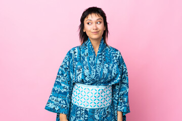 Young woman wearing kimono over isolated blue background making doubts gesture looking side
