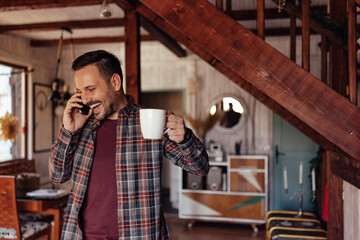 Positive man, talking over the phone, laughing while holding a cup of coffee.