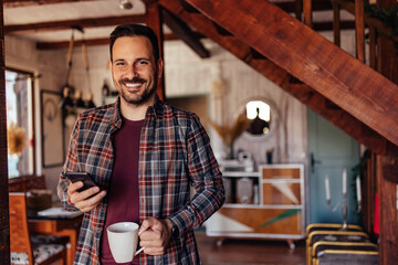 Portrait of an adult man, looking at the camera while holding coffee and phone.