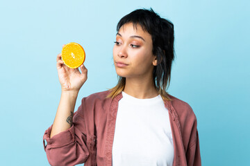 Young Uruguayan woman over isolated blue background holding an orange