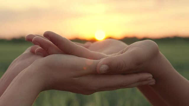 Happy people hold sunset in their hands. Prayer at sunset. Children's hands against sky. Concept of help and love for your neighbor. Religion, sunshine lifestyle.