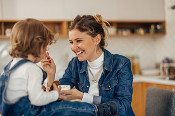 Young mom laughing with her toddler, holding a cup, feeding her