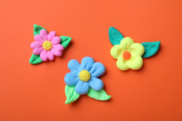 Colorful flowers with leaves made from play dough on orange background, flat lay