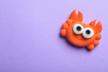 Colorful crab made from play dough on violet background, top view. Space for text