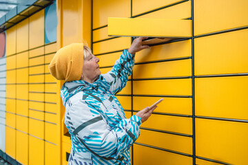 Caucasian woman picks up mail from automated self-service post terminal machine. Mail shipping...