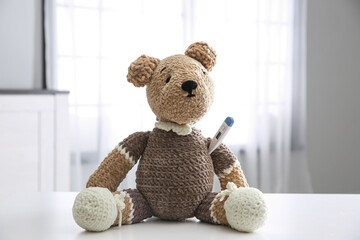Cute toy bear with thermometer on white table indoors. Children's hospital