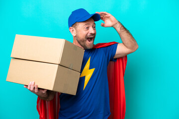Super Hero delivery man isolated on blue background doing surprise gesture while looking to the side