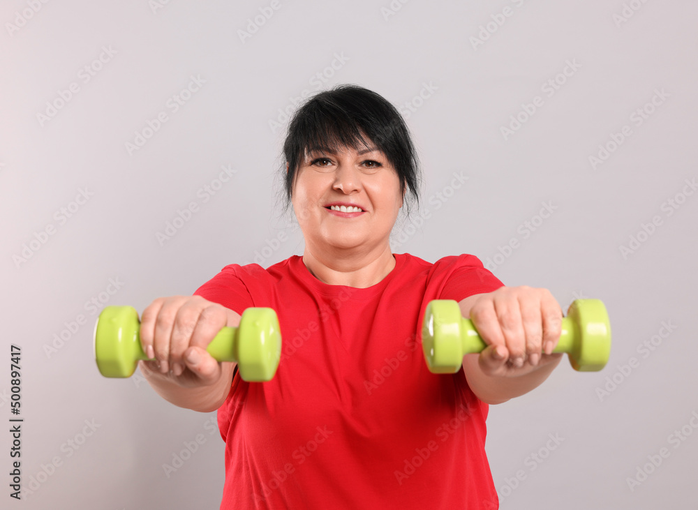 Canvas Prints Happy overweight mature woman doing exercise with dumbbells on grey background