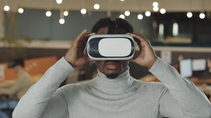 Office male worker wearing a VR headset, virtual reality concept. Portrait african american software developer standing in office room. It, business and new technologies concept - Powered by Adobe
