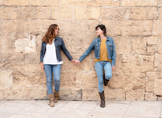 a lesbian couple holding hands leaning against a wall, gay concept