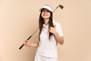 Young Ukrainian girl isolated on beige background playing golf and with thumbs up because something good has happened