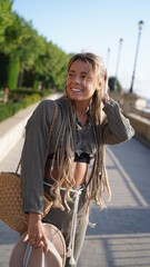 Portrait of a smiling girl with dreadlocks. Bohemian woman in boho style holding a hat. A charming girl with freckles in a hat smiles and laughs merrily. Bright and beautiful smile, street style.
