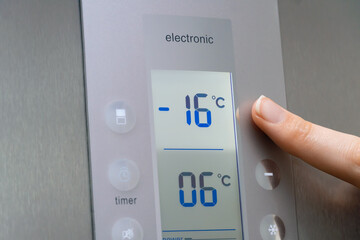 Close-up of a woman's hand regulates the temperature of the refrigerator freezer. Stylish modern...