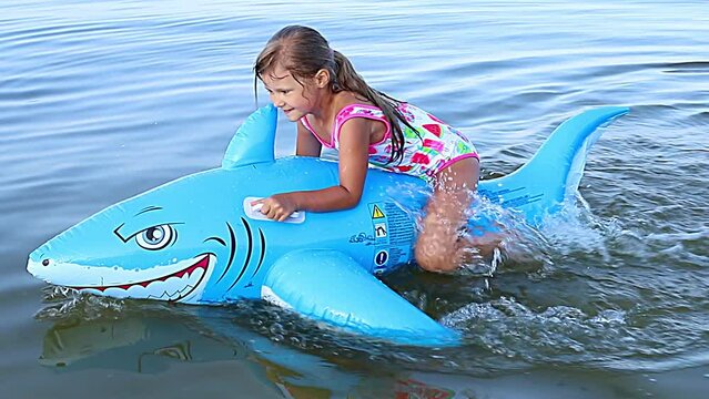 Happy girl swimming on an inflatable shark toy in the sea