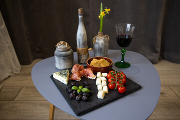 Glass of wine, meat board with prosciutto, blue cheese, cheese, tomato cherry and snacks in interior on the table