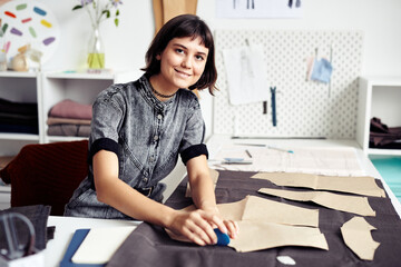 Smiling young seamstress outlining and cutting out garment details