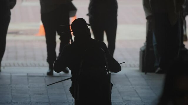 Close up silhouetted man plays violin for passing people in New York Central Park