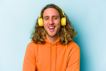 Young caucasian man listening to music isolated on blue background laughing and having fun.