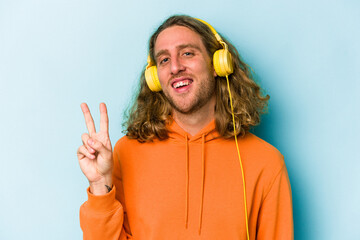 Young caucasian man listening to music isolated on blue background joyful and carefree showing a peace symbol with fingers.