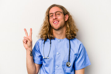 Young nurse caucasian man isolated on blue background joyful and carefree showing a peace symbol with fingers.