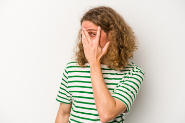 Young caucasian man isolated on white background blink at the camera through fingers, embarrassed covering face.