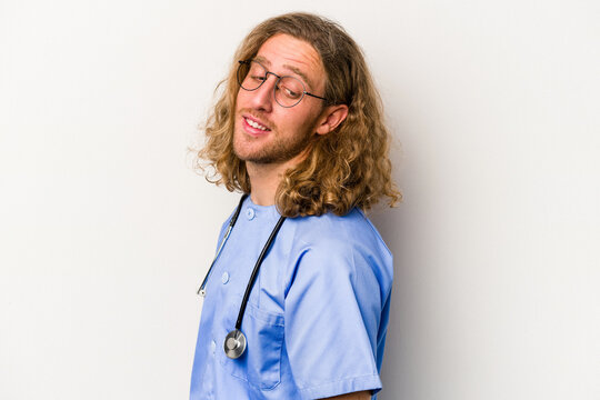 Young nurse caucasian man isolated on blue background looks aside smiling, cheerful and pleasant.