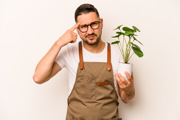 Hispanic gardener man holding a plant isolated on white background showing a disappointment gesture...