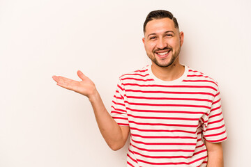 Young hispanic man isolated on white background showing a copy space on a palm and holding another...