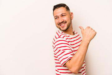 Young hispanic man isolated on white background points with thumb finger away, laughing and carefree.