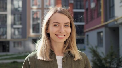 Pretty girl looking at camera with lively emotion while enjoying sunny weather outdoors. Close up face of beautiful blond sexy smiling woman with long hair and blue eyes. Female charming smile.