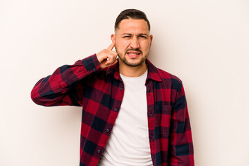 Young hispanic man isolated on white background covering ears with fingers, stressed and desperate by a loudly ambient.