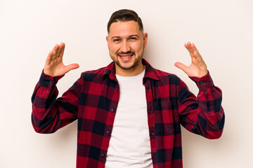 Naklejka premium Young hispanic man isolated on white background holding something with palms, offering to camera.