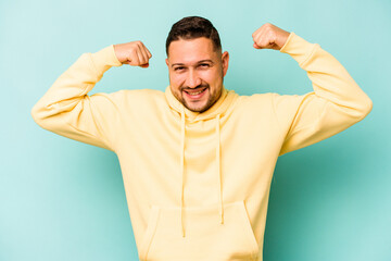 Young hispanic man isolated on blue background showing strength gesture with arms, symbol of feminine power