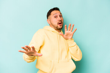 Young hispanic man isolated on blue background being shocked due to an imminent danger