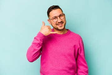 Young hispanic man isolated on blue background showing a mobile phone call gesture with fingers.