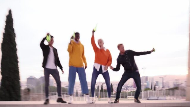 Group of diverse people dancing playfulness outdoors drinking beer and having fun. Happy friends celebrating together the success. Happiness and friendship concept