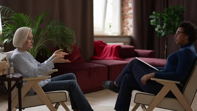 Woman client is telling story and psychoanalyst listening to her during psychotherapy in room spbas. 4k Mature Caucasian female shares problem and gestures with hands, experienced psychologist listens