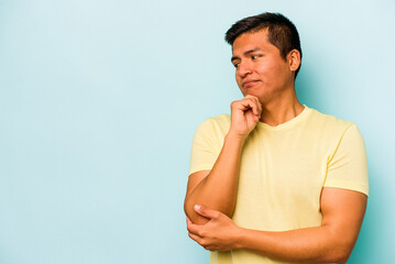 Young hispanic man isolated on blue background looking sideways with doubtful and skeptical expression.