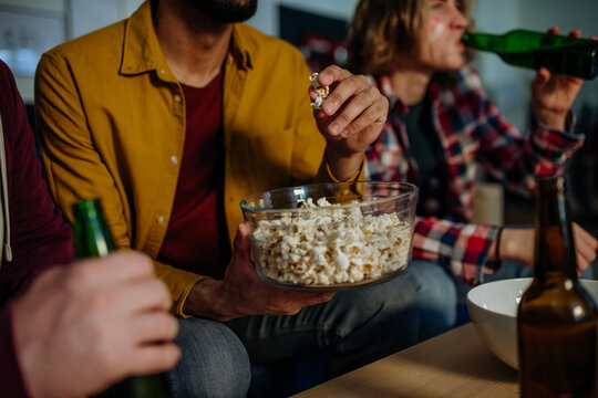 Close-up of football fans friends watching match and eating popcorn.